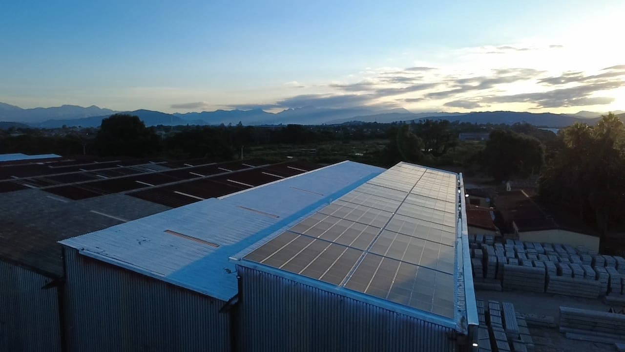 Solar panels on a long industrial roof at dusk, with mountains on the horizon